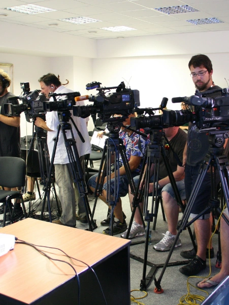 Group of individuals in a room, each with a camera, capturing media coverage for press releases.